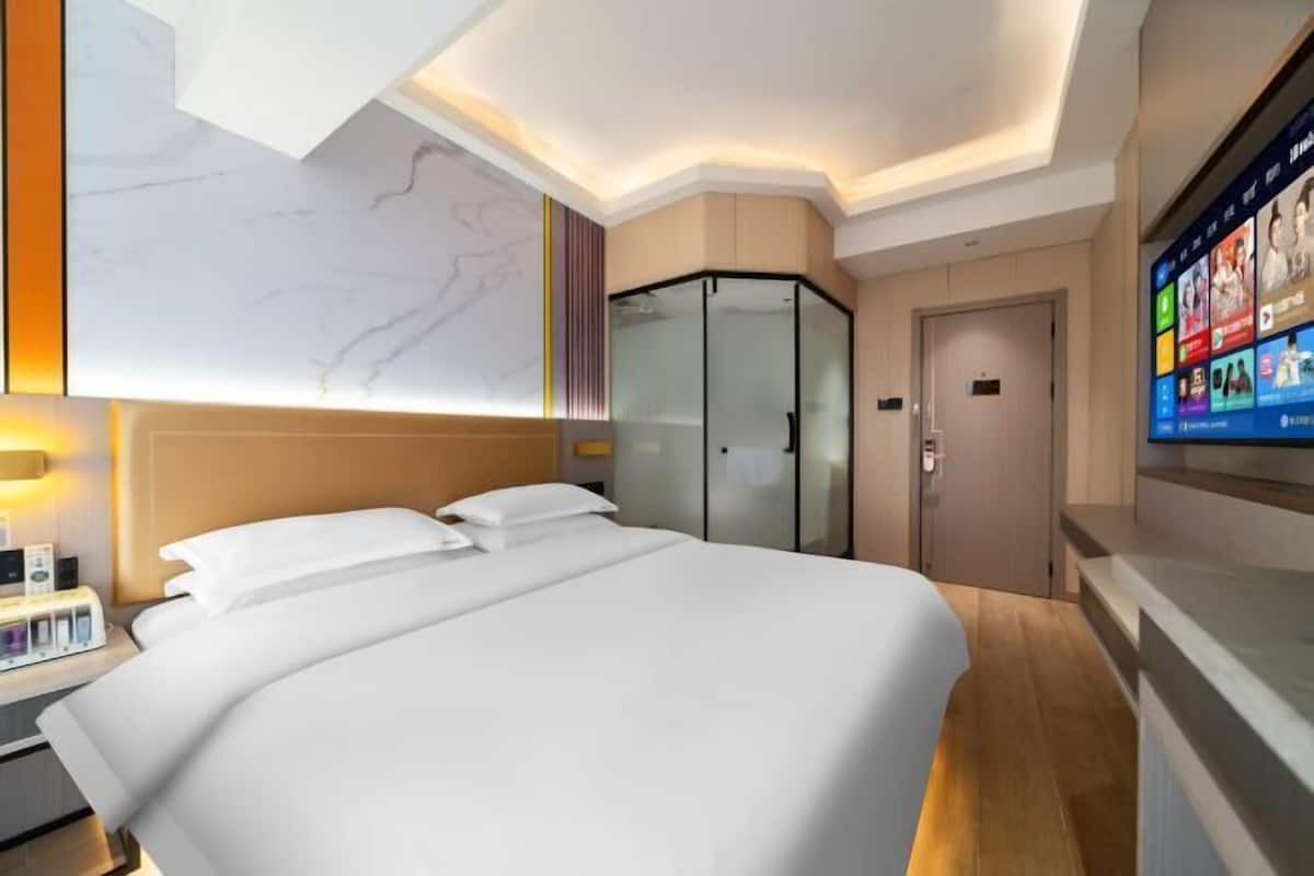 A modern hotel room with a large bed, a wardrobe, a television, and a marble wall.