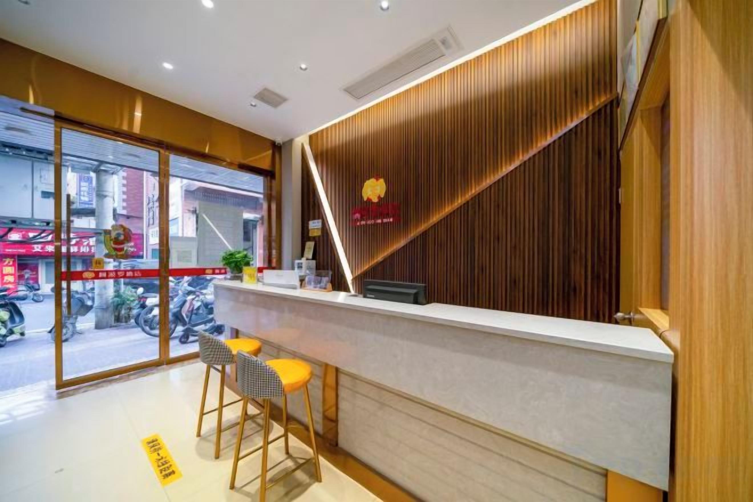 Zona de recepción con mostrador, dos taburetes de bar y un panel de pared de madera.
