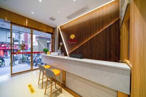 Zona de recepción con mostrador, dos taburetes de bar y un panel de pared de madera.