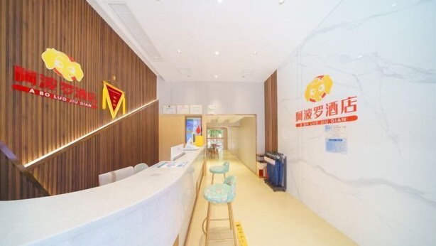 A hotel reception area with a wooden reception desk, a counter, and a seating area with stools. There are signs on the wall with the hotel's logo and name. - Apollo Hotel (Zhangzhou Ancient City) (Zhangzhou)