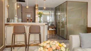 Een moderne keuken met een bar, twee barkrukken, een eettafel met bloemen en een bank met een geruit kussen.