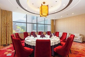 A conference room with a round table, red chairs, and a view of mountains through large windows. - Ju Xiu Hotel (Zhen'an)