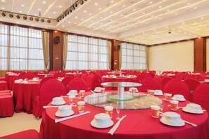 A banquet hall with round tables set for dining, large windows, and a stage. - Ju Xiu Hotel (Zhen'an)