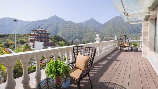 Een balkon met een rieten stoel, een hangstoel en uitzicht op bergen en een pagode.