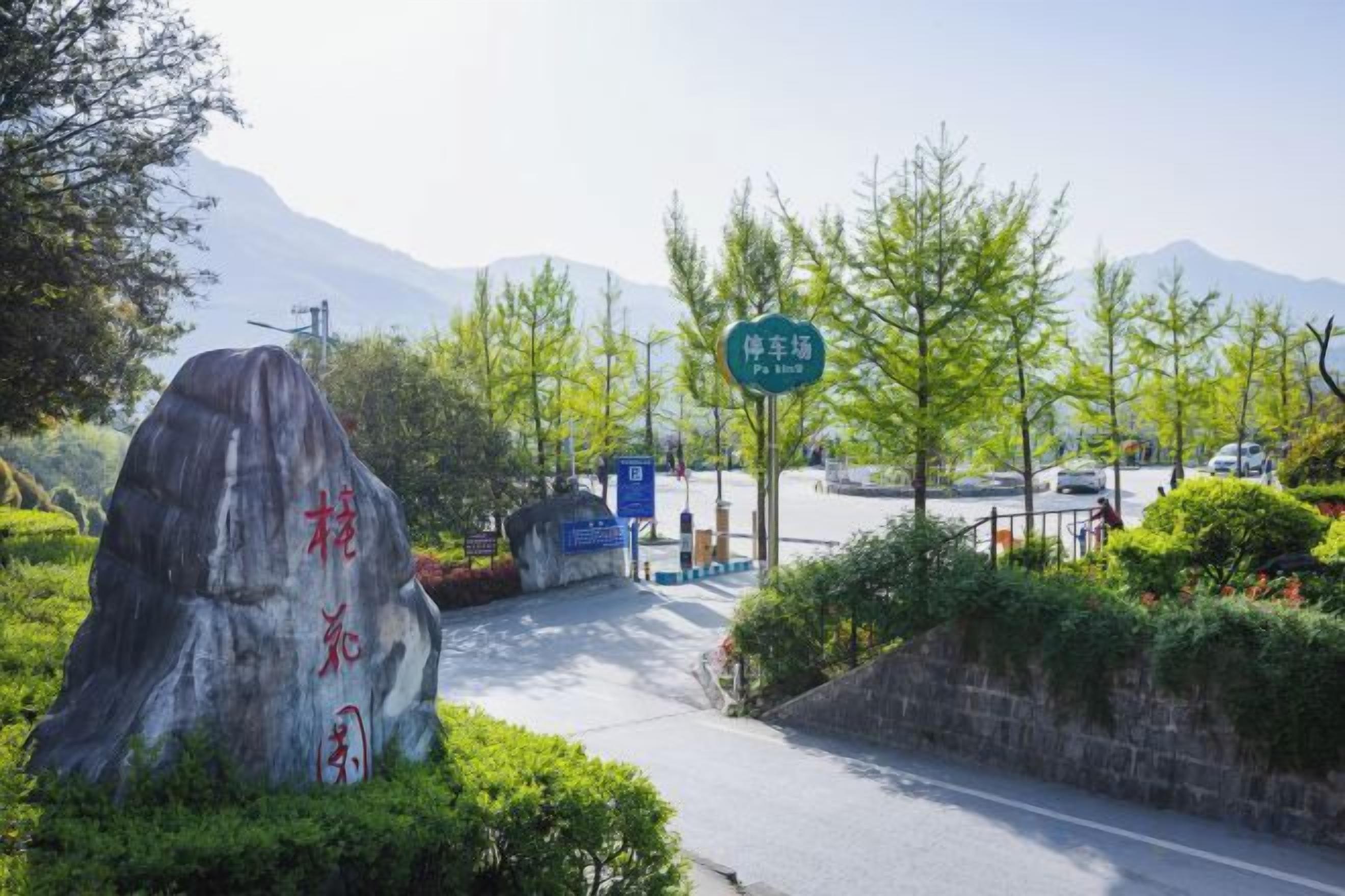 Un área de estacionamiento con una roca grande, un letrero y una montaña al fondo.