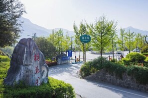 A parking area with a large rock, a sign, and a mountain in the background. - Ju Xiu Hotel (Zhen'an)