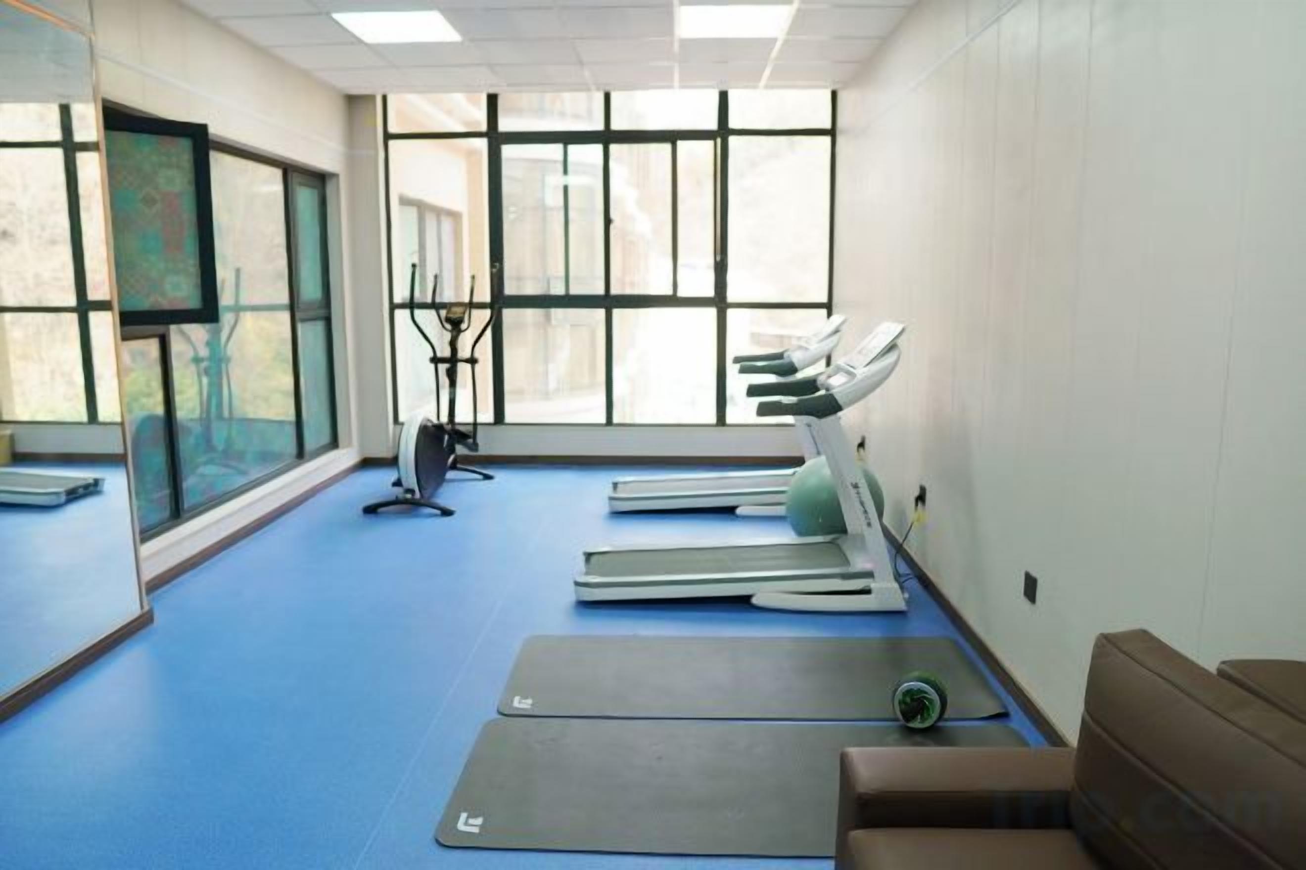 Een kamer met fitnessapparatuur, een loopband en een groot raam.