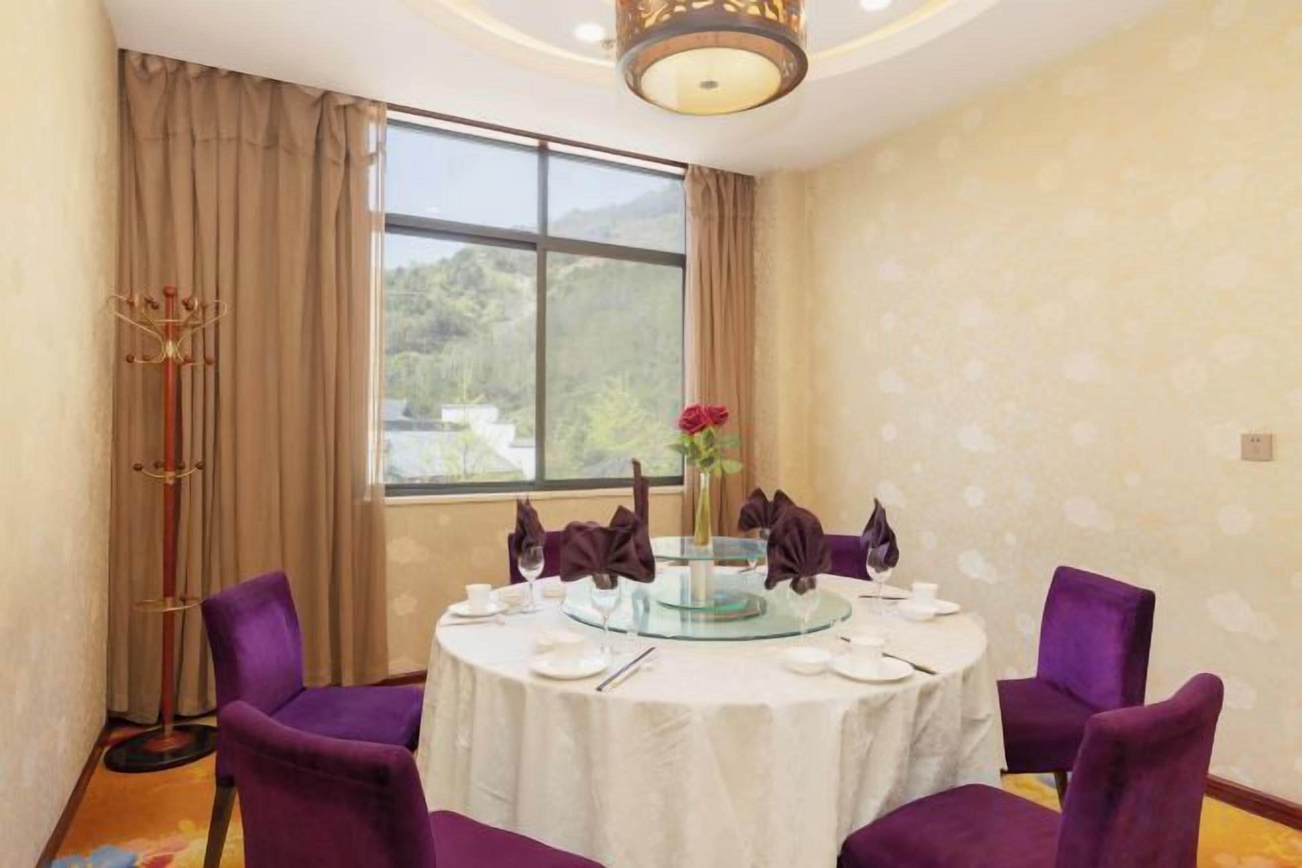 A dining area with a round table, purple chairs, and a view of the outdoors through a large window.