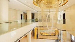 Een ruime lobby met een weelderige kroonluchter, een glazen balustrade en een patroonvloer.