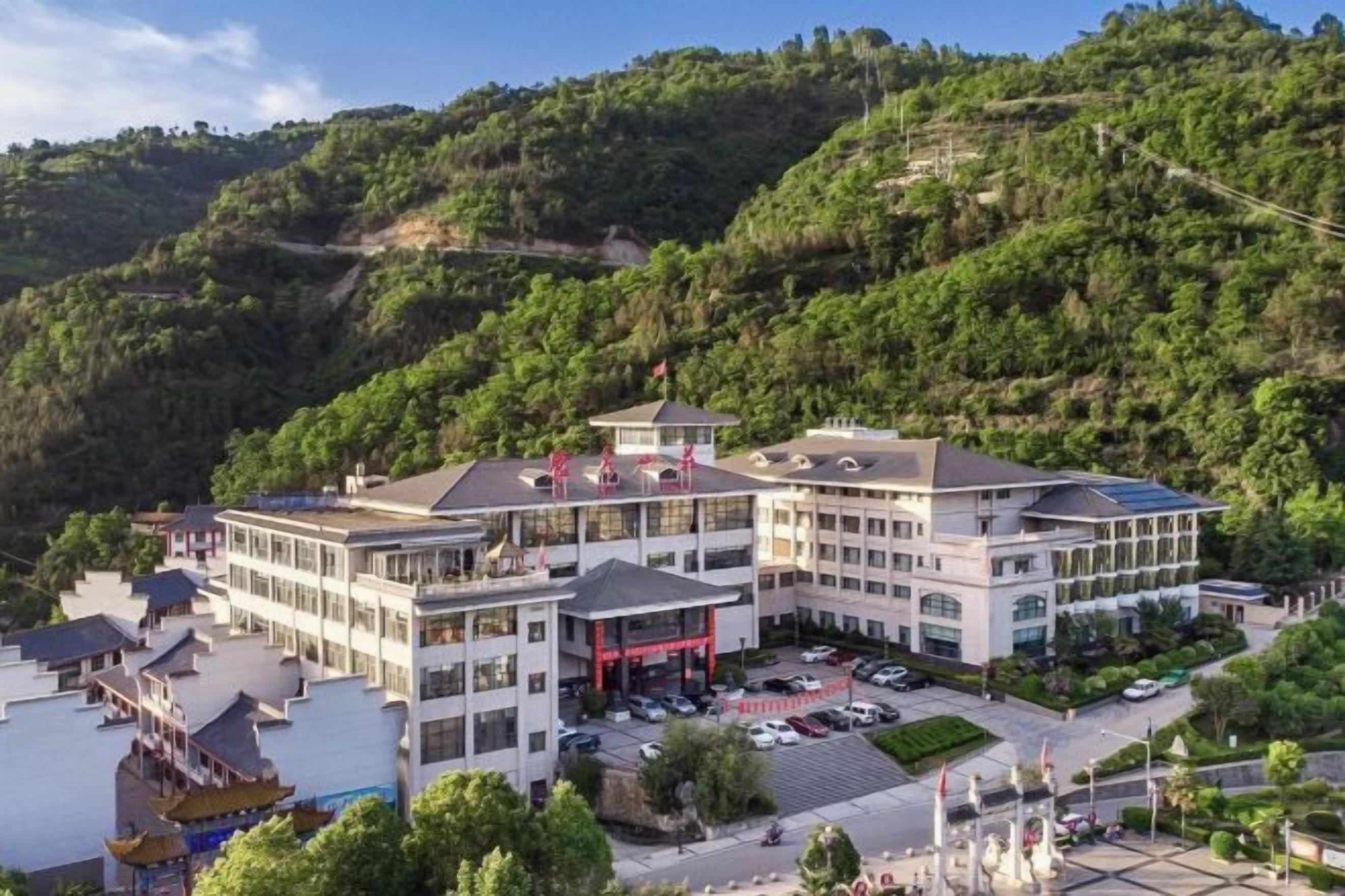 Un hotel de varios pisos con estacionamiento y vistas a un paisaje montañoso.