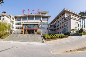 A multi-story building with a central entrance, surrounded by a landscaped area with steps leading up to the entrance. - Ju Xiu Hotel (Zhen'an)