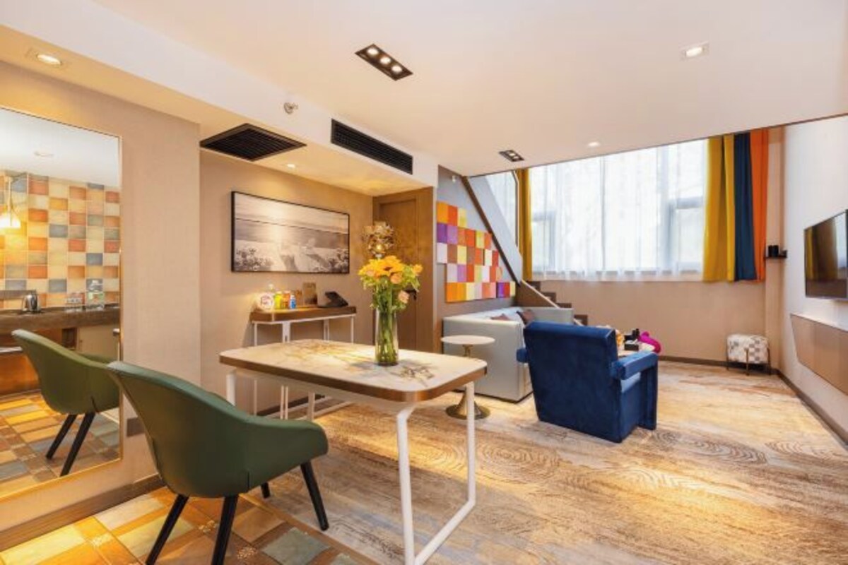 Una camera d'albergo moderna con angolo ristoro, divano, televisore e un'ampia finestra.