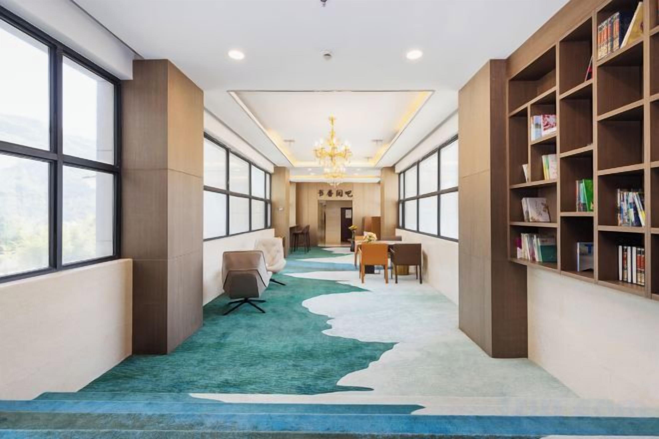 Un pasillo de hotel con piso alfombrado, un candelabro, una zona de estar y estanterías.