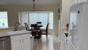 A kitchen with white cabinets, a dishwasher, a refrigerator, and a dining area with a table and chairs.