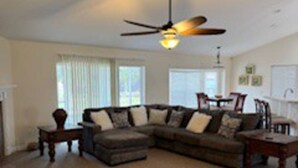 A living room with a sectional sofa, a dining table, and a ceiling fan.