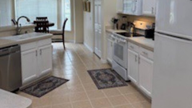 A spacious kitchen with white cabinets, a dishwasher, a refrigerator, and a stove.