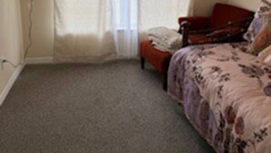 A bedroom with a bed, a television, and a window with curtains.