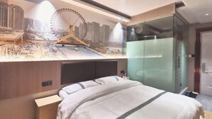 Una habitación de hotel con cama, armario y un mural en la pared que muestra un paisaje urbano con noria.