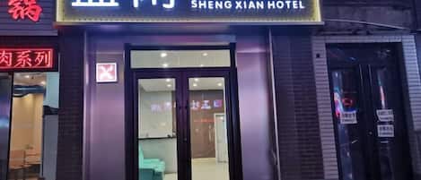 A hotel entrance with a sign reading 'SHENG XIAN HOTEL' and a neon sign above.