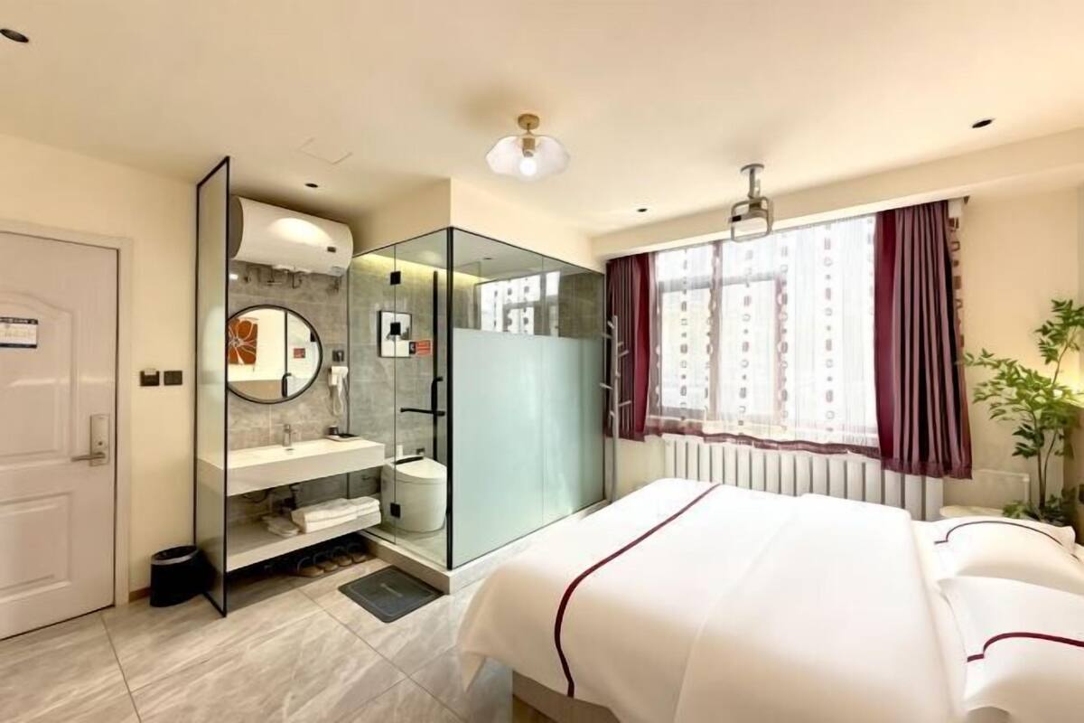 Ein Hotelzimmer mit Bett, einer gläsernen Dusche, einem weißen Waschbecken und einem Vorhangfenster.