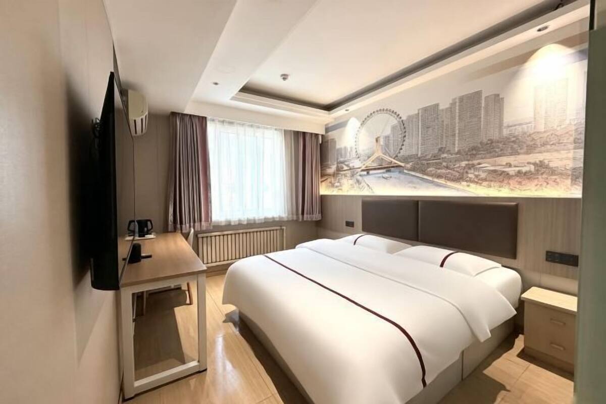 Ein modernes Hotelzimmer mit einem großen Bett, einem Schreibtisch, einem Flachbildfernseher und einer Stadtansicht als Wandgemälde.