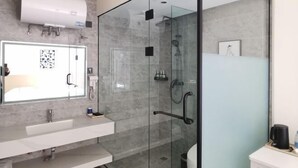 Un baño moderno con ducha de vidrio, un espejo grande y un lavabo blanco.