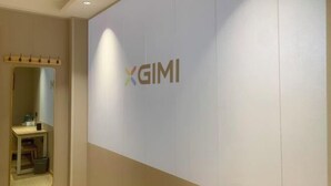 Una habitación con un letrero grande en la pared que dice "XGIMI" y un escritorio pequeño con un espejo y algunos objetos encima.