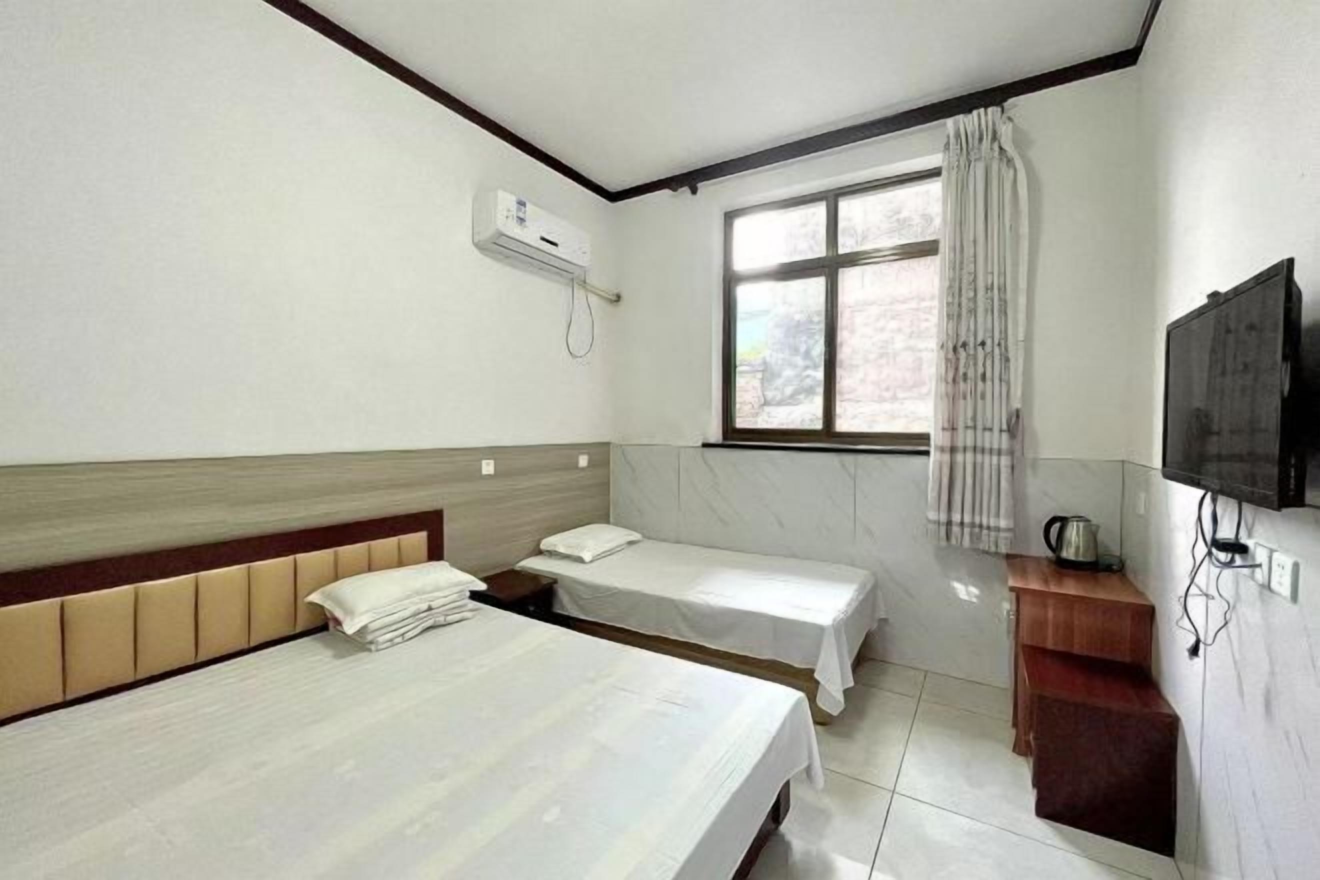A hotel room with two beds, a window with curtains, a television, and a small wooden table.