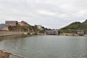 A calm river with buildings on the banks, including a multi-story structure and a smaller building with a balcony.