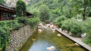 A traditional Japanese-style building with a stone wall and wooden deck along a river.