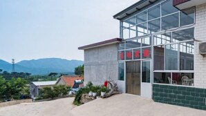 A building with large windows, a visible sign with red characters, and a paved area with plants. - Yuming Farmhouse (Tianjin)