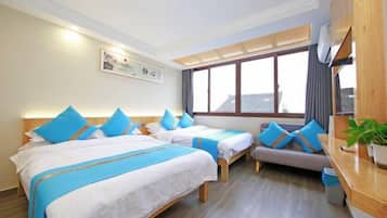 Habitación de hotel con dos camas, un sofá, un escritorio de madera y un ventanal grande.