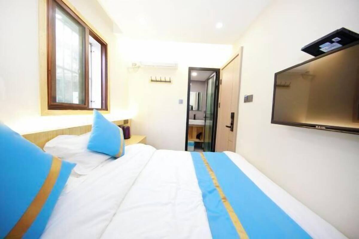 Een hotelkamer met een bed, een aan de muur bevestigde televisie en een raam.