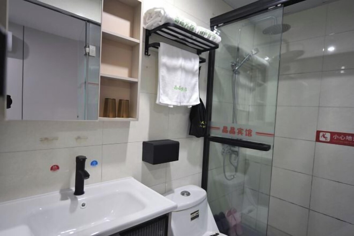 Un baño moderno con lavamanos blanco, cabina de ducha con mampara de vidrio y toallero con toallas dobladas.