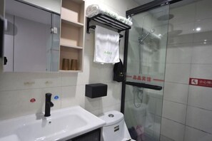 Un baño moderno con lavamanos blanco, cabina de ducha con mampara de vidrio y toallero con toallas dobladas.