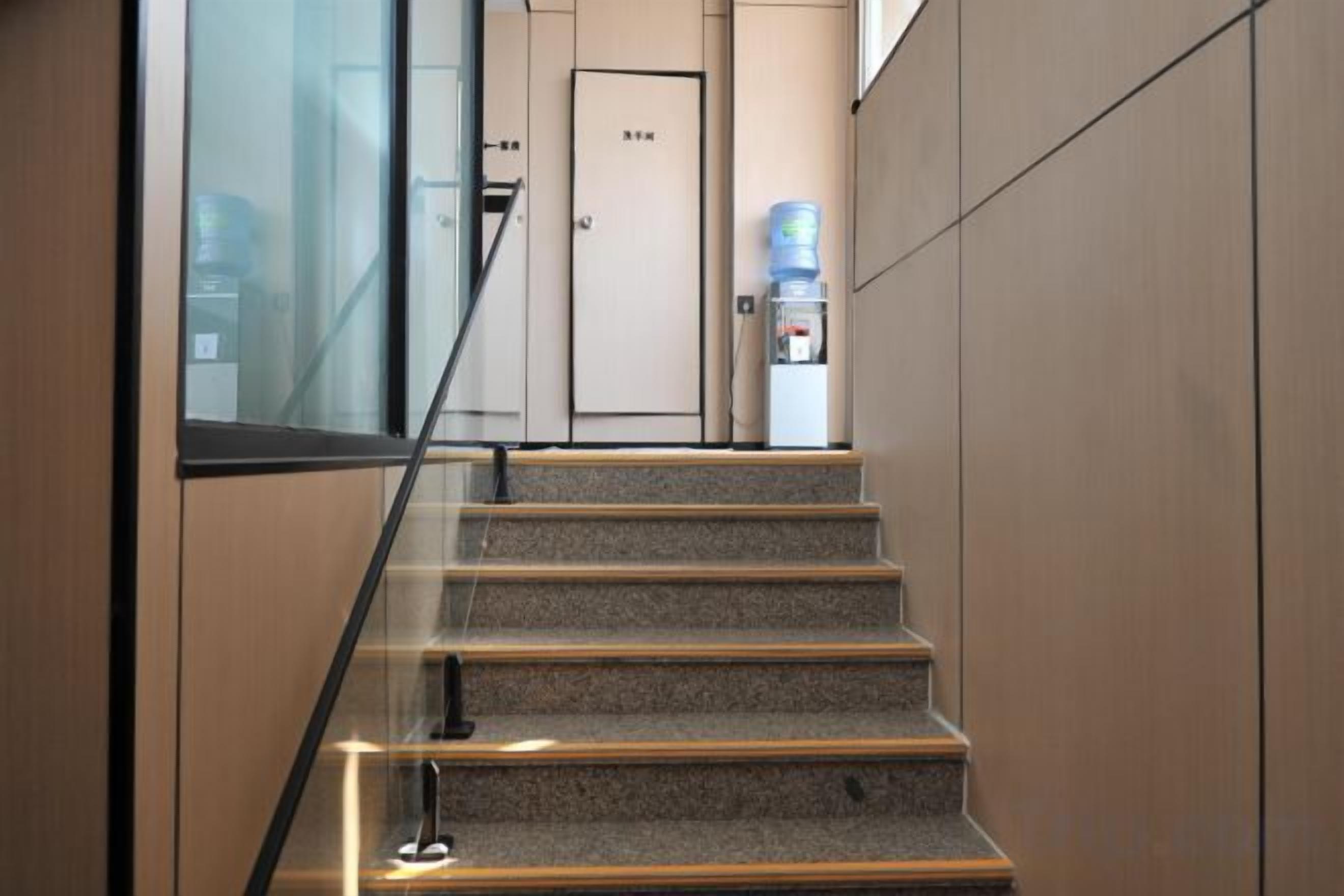 A staircase with a glass railing leading to a door with a water dispenser nearby.