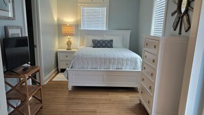 A bedroom with a bed, dresser, nightstand, TV, and a ceiling fan.