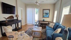 A spacious living room with a blue sofa, patterned armchair, wooden coffee table, and a TV mounted on the wall.