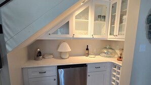 A compact kitchen with white cabinetry, a stainless steel dishwasher, and a wooden floor.