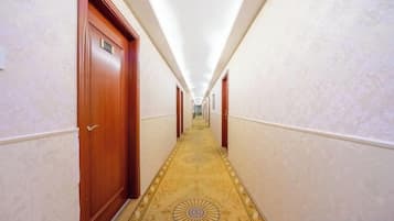 Corredor de hotel com portas de madeira, carpete estampado e luminária no teto.