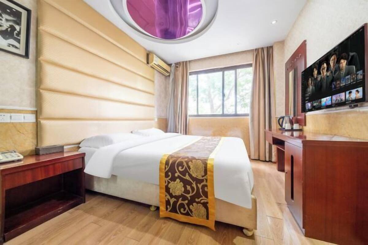 Une chambre d’hôtel avec un lit, une table de chevet en bois, une télévision et une fenêtre avec des rideaux.