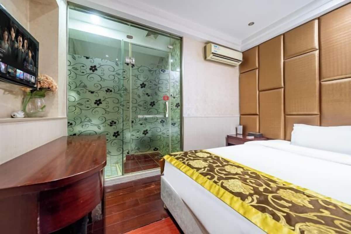 Une chambre d’hôtel équipée d’un lit, d’un bureau, d’une porte en verre ornée de motifs floraux et d’un appareil de climatisation.
