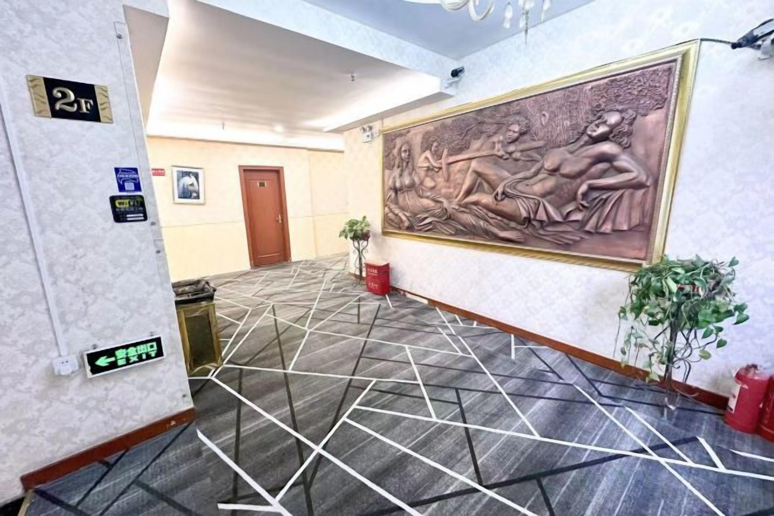Un vestíbulo de hotel con alfombra estampada, una escultura grande en la pared y una puerta al fondo.