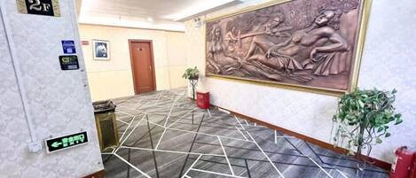 Un vestíbulo de hotel con alfombra estampada, una escultura grande en la pared y una puerta al fondo.