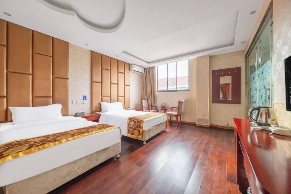 Une chambre d’hôtel avec deux lits, un bureau, une chaise, une fenêtre et un téléviseur fixé au mur.