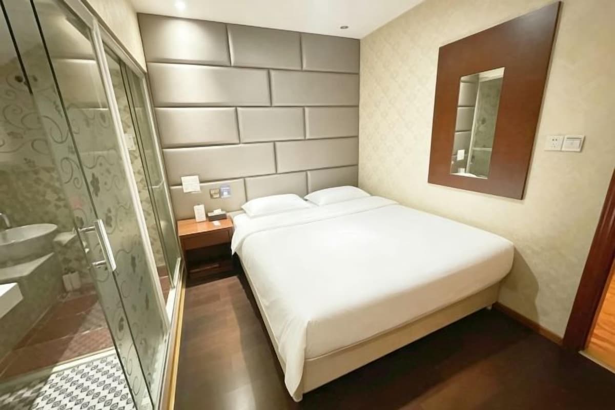 Quarto de hotel com uma cama grande, mesa de cabeceira, espelho e área de chuveiro.