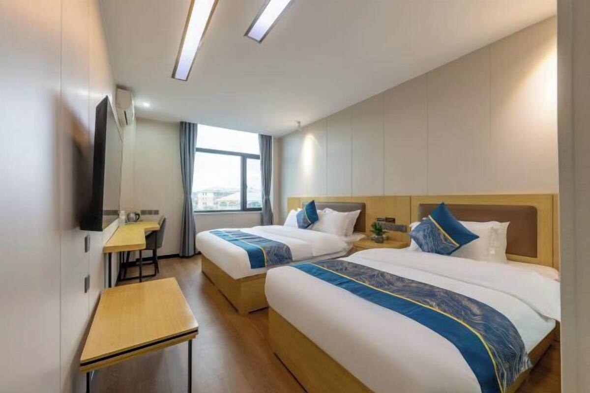 A hotel room with two beds, a desk, a TV, and a window with a view.