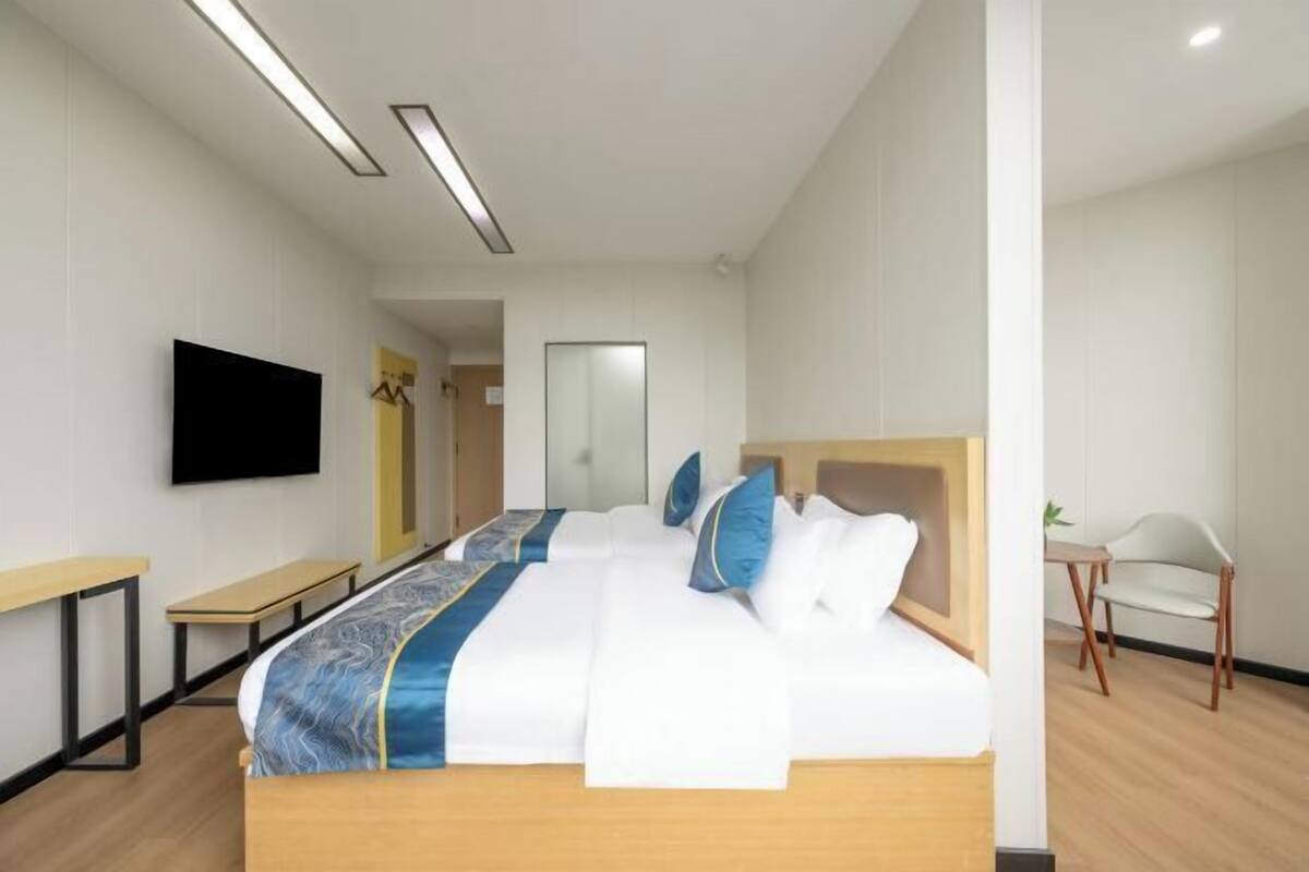 A hotel room with a large bed, a flat-screen TV mounted on the wall, a mirror, and a small table with a chair.
