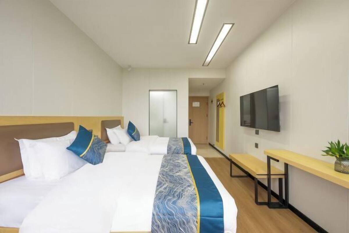 A hotel room with a large bed, a TV mounted on the wall, and a bench by the window.