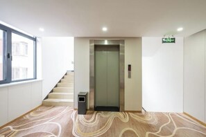 An elevator in a hallway with a patterned carpet, a trash bin, and a sign indicating the direction to the lobby. - Shankee Express Hotel (Beijing Miyun Guoyuan) (Beijing)